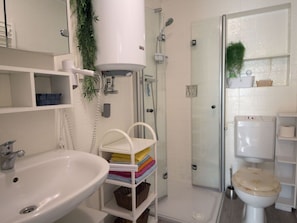 Ein Badezimmer mit Waschbecken, Toilette, Dusche und Regalen mit Handtüchern.