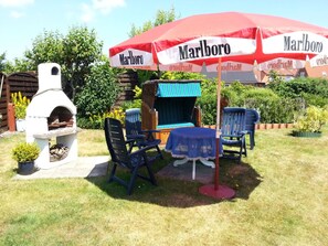 Ein Außenbereich mit Sitzgelegenheit, Grill, Stühlen und Tisch unter einem großen rot-weißen Sonnenschirm.