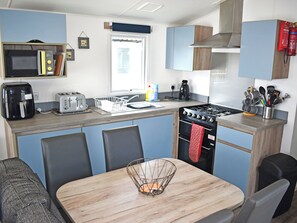 A compact kitchenette with a microwave, toaster, sink, stove, and a small dining area with chairs and a table. - 3 bedroom accommodation in Budleigh Salterton (Budleigh Salterton)