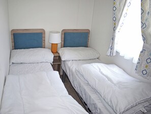 A twin room with two beds, a nightstand with a lamp, and a window with curtains. - 3 bedroom accommodation in Budleigh Salterton (Budleigh Salterton)