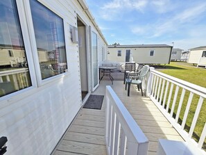A covered outdoor area with a wooden deck, a white railing, and a seating area with a table and chairs. - Foreshore 1 at Seashore Holiday Park (Caister-On-Sea)