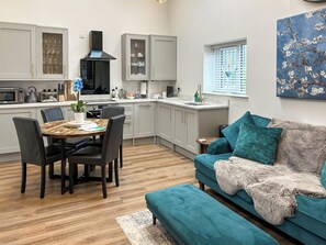 A modern kitchen with grey cabinets, a dining table with chairs, a teal sofa, and a painting on the wall. - Merlyn Barn - UKC9439 (Holmesfield)