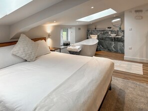 A modern bedroom with a large bed, a skylight, a bathroom with a bathtub, and a marble backsplash. - Merlyn Barn - UKC9439 (Holmesfield)