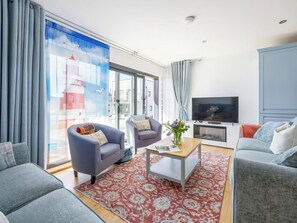 Ein modernes Wohnzimmer mit einer Couch, Sesseln, einem Couchtisch und einem Fernseher.