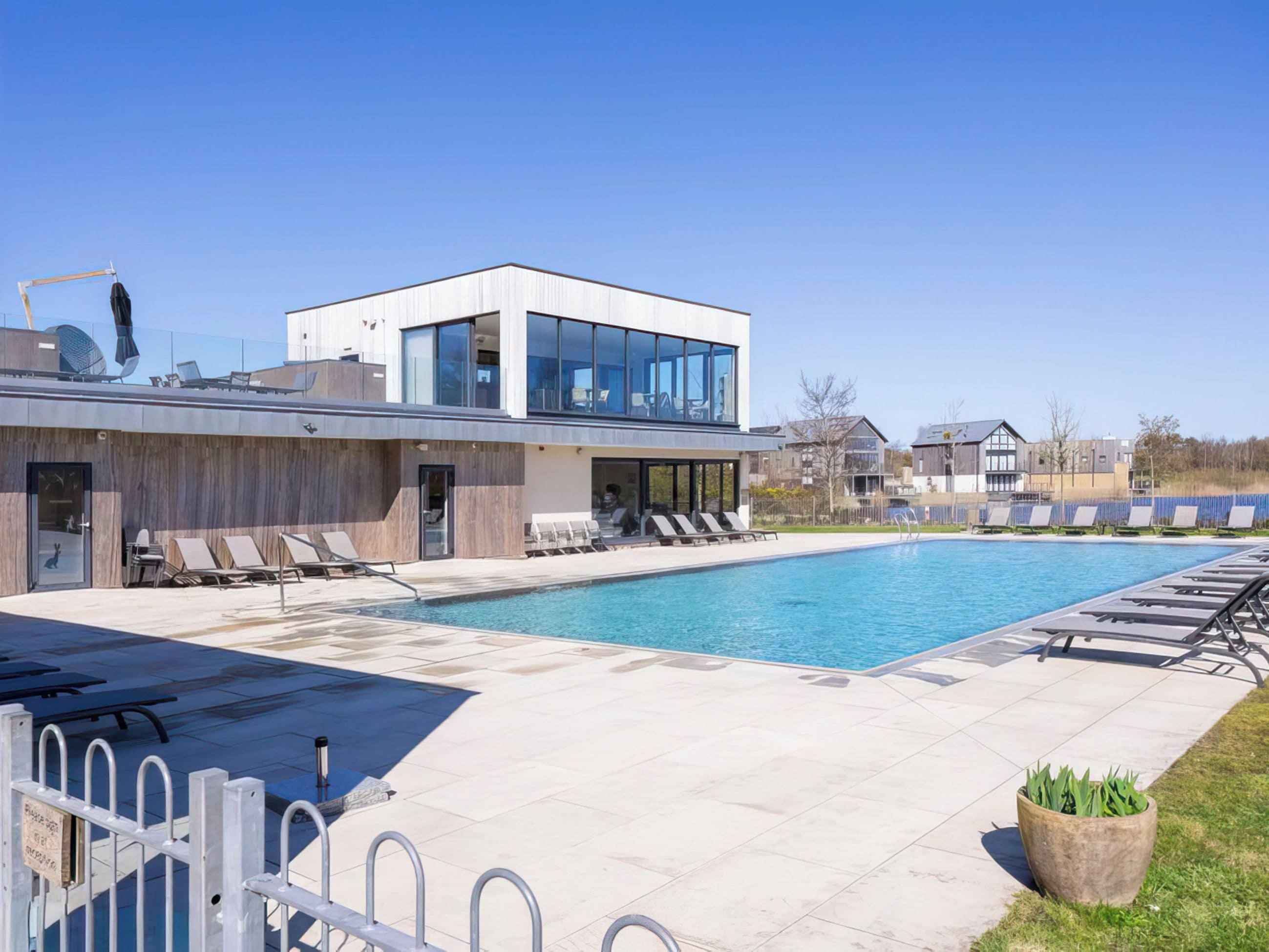 A modern building with a swimming pool, lounge chairs, and a clear sky.