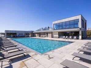 Ein moderner Poolbereich im Freien mit Liegestühlen und einem Gebäude mit großen Fenstern.