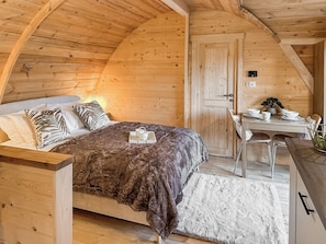 Ein gemütliches Schlafzimmer mit Holzbalkendecke, einem Bett mit flauschiger Decke, einem Nachttisch mit Pflanze und einem kleinen Schreibtisch mit Stühlen.