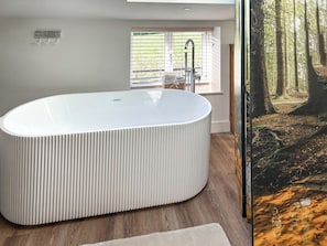A modern bathroom with a freestanding bathtub, a window with blinds, and a view of a forest. - Forest Barn - UKC9438 (Holmesfield)