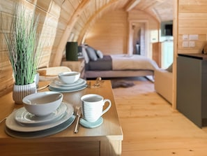 A cozy interior with a wooden dining table set with plates, bowls, and a cup, a bed with pillows, and a television in a room with wooden walls and a sloped ceiling. - Laurel Lodge - UKC9519 (Gillingham, near Beccles)