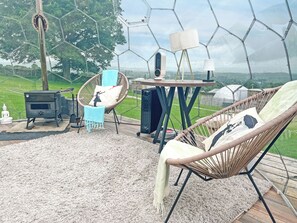 A cozy outdoor seating area with a hexagonal glass enclosure, a wood-burning stove, and a comfortable chair with cushions. - Ingleborough Dome - UKC9594 (Clitheroe and the Ribble Valley)
