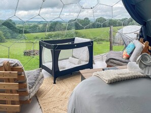 A room with a view of a green landscape, a black and white baby playpen, a wooden chair, and a bed with a white blanket. - Malham Dome - UKC9597 (Earby)