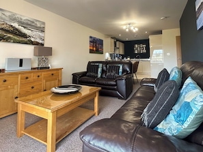A living room with a sofa, a coffee table, and a dining area with a chair. - 2 bedroom accommodation in Whitby (Whitby)