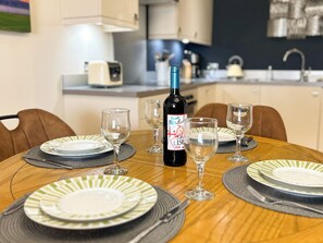 A dining table set with plates, glasses, and a bottle of wine, with chairs around it. - 2 bedroom accommodation in Whitby (Whitby)