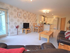 A living room with a sofa, a TV, a dining table with chairs, and a kitchen area in the background. - 2 bedroom accommodation in Whitby (Whitby)