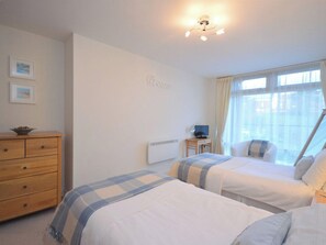 A bedroom with two beds, a dresser, a desk with a computer, and a window with curtains. - 2 bedroom accommodation in Whitby (Whitby)