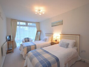 A bedroom with two beds, a desk with a computer, a window with curtains, and a painting on the wall. - 2 bedroom accommodation in Whitby (Whitby)