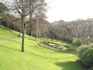 A park with a grassy hill, trees, and a circular garden. There are buildings in the background. - 2 bedroom accommodation in Whitby (Whitby)