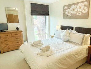 A bedroom with a bed, a dresser, a television, and a window with a view of a brick wall. - 2 bedroom accommodation in Whitby (Whitby)