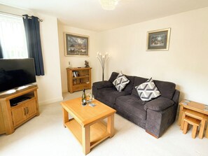 A living room with a sofa, coffee table, TV stand, and a bookshelf. - 2 bedroom accommodation in Whitby (Whitby)