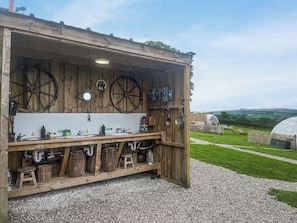 A rustic wooden outdoor kitchen with a sink, stools, and a view of the countryside. - Weets Hill Dome - UKC9598 (Earby)