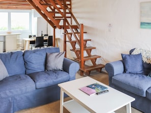 A living room with two sofas, a white coffee table, and a wooden staircase. - 2 bedroom accommodation in Llanengan (Llanengan)