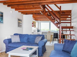 A living room with a blue sofa, a white coffee table, and a wooden staircase. - 2 bedroom accommodation in Llanengan (Llanengan)