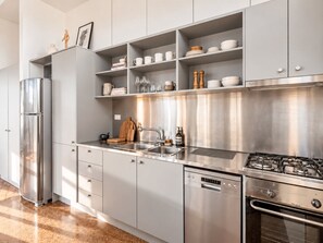A modern kitchen with stainless steel appliances, a dishwasher, and a built-in oven. - Balcony 1-Bed Apartment Near Sydney Road (Brunswick)