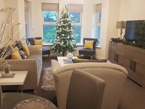 Ein Wohnzimmer mit Weihnachtsbaum, beigen Sofas, einem Couchtisch und einem Kamin.