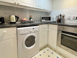 A compact kitchen with a washing machine, microwave, and oven. - 2 bedroom accommodation in Whitby (Whitby)