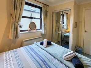 A bedroom with a bed, a window with curtains, a mirror, and a door leading to another room. - 2 bedroom accommodation in Whitby (Whitby)