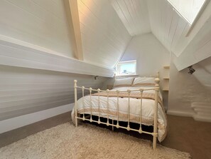 A bedroom with a sloped ceiling, a bed with a white frame, a fluffy rug, and a window with a view of the sky. - 1 bedroom accommodation in Whitby (Whitby)