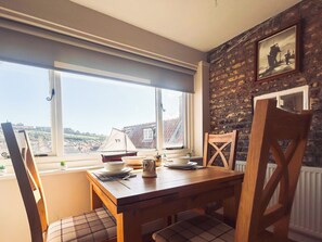 A dining area with a table, chairs, and a view of a town through large windows. - 1 bedroom accommodation in Whitby (Whitby)