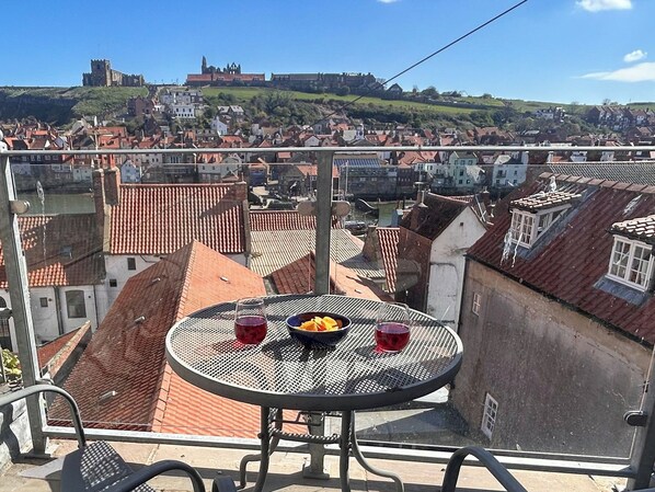 Un balcon avec une table ronde, une chaise et une vue sur un paysage urbain, avec des bâtiments et une structure située au sommet d’une colline.