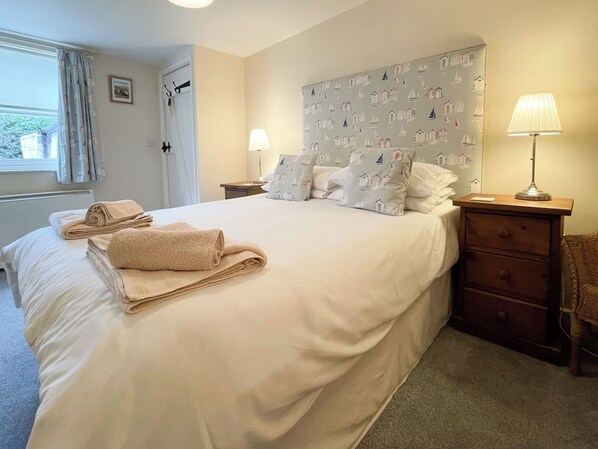 A neatly made bed with rolled towels, a headboard with a sailboat pattern, two bedside lamps, and a wooden nightstand with drawers. - 2 bedroom accommodation in Whitby (Whitby)
