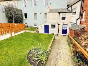 A courtyard with a lawn, a wooden fence, and a small garden area with plants. - 2 bedroom accommodation in Whitby (Whitby)