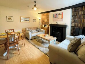 A living room with a fireplace, a bookshelf, and a dining area with chairs and a table. - 2 bedroom accommodation in Whitby (Whitby)