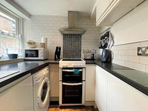 A compact kitchen with a washing machine, microwave, stove, and oven. - 2 bedroom accommodation in Whitby (Whitby)
