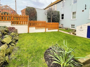 A well-maintained garden with a wooden fence, a stone wall, and a small building with a blue door. - 2 bedroom accommodation in Whitby (Whitby)