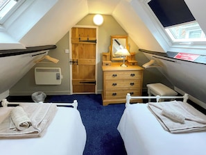 Une petite chambre mansardée, chaleureuse et accueillante, avec deux lits, une commode, un miroir et une fenêtre de toit.