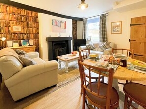 A cozy living room with a fireplace, a dining table set for a meal, and a bookshelf filled with books. - 2 bedroom accommodation in Whitby (Whitby)