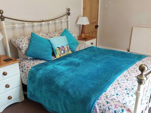 Una cama con edredón estampado de flores, una manta color turquesa y dos almohadas, una con estampado colorido.