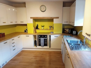 A compact kitchen with white cabinets, a yellow backsplash, a built-in oven, a dishwasher, and a sink. - 4 bedroom accommodation in Whitby (Whitby)
