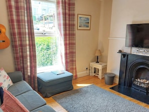 Una sala de estar con sofá, reposapiés, chimenea, televisión y ventana con cortinas.