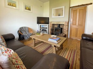 A living room with a sofa set, a wooden coffee table with books, a television, a fireplace, and a door. - 3 bedroom accommodation in Whitby (Whitby)
