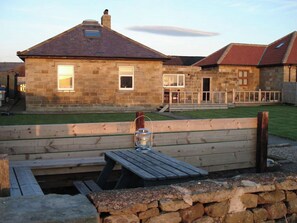 A stone house with a sloped roof, a wooden deck, and a stone wall. - 3 bedroom accommodation in Whitby (Whitby)