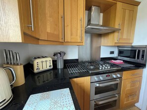 A kitchen with wooden cabinets, a gas stove, a microwave, and a toaster. - 3 bedroom accommodation in Whitby (Whitby)