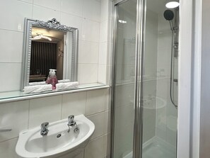 Une salle de bain dotée d’une douche à parois de verre, d’un lavabo à deux robinets et d’un miroir encadré d’un cadre orné.