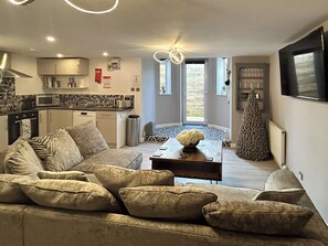 Ein modernes Wohnzimmer mit einer Couch, einem Couchtisch und einer Küche im Hintergrund.
