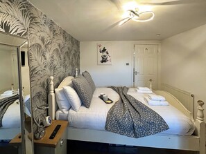 Habitación de hotel con cama, mesita de noche, espejo y pared decorada con un estampado floral.