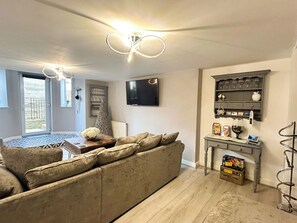 A living room with a sofa, a coffee table, a television, and a wine rack. - 2 bedroom accommodation in Whitby (Whitby)